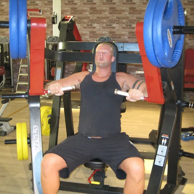 Mann sitter i treningsapparat og trener bryst