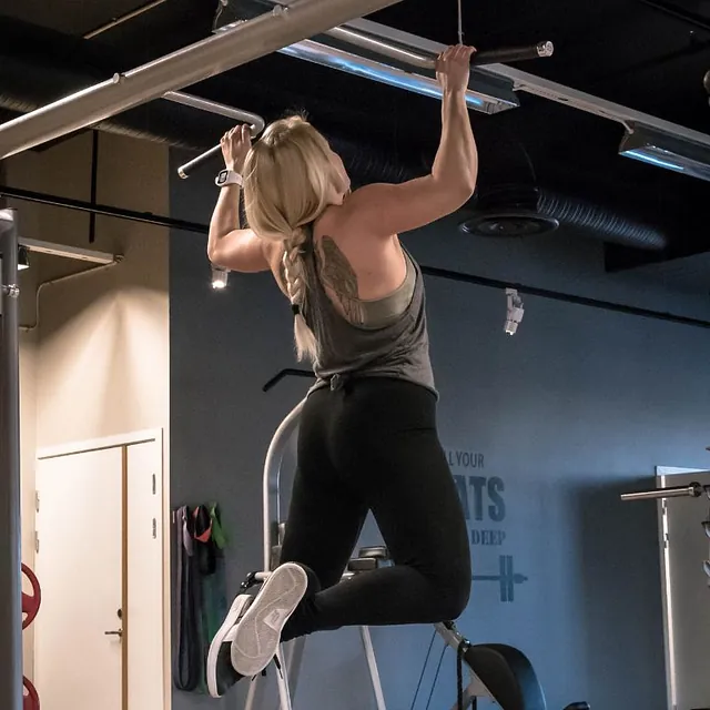 Jente med tatovering på ryggen tar pullups