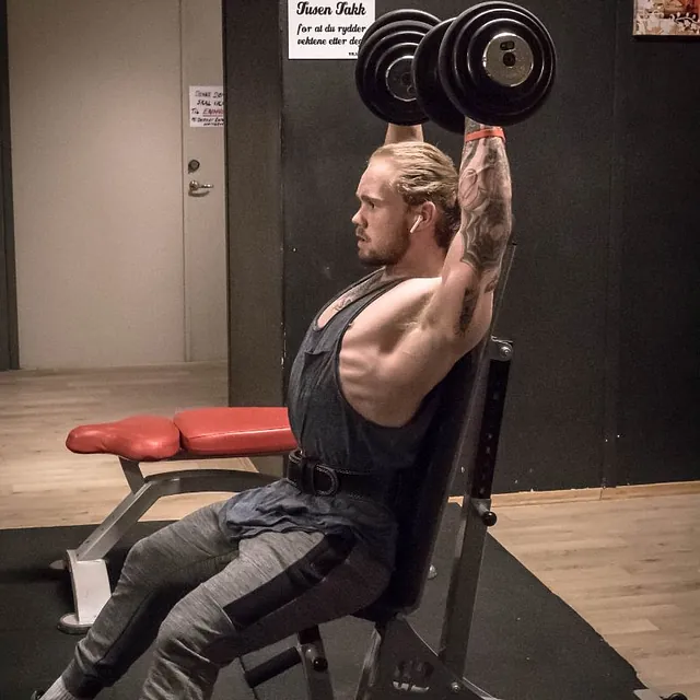 Mann med øreplugger sitter på benk og løfter manualer over hodet
