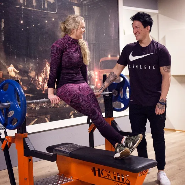 Jente sitter på benkpress-stangen prater med mann som ser på